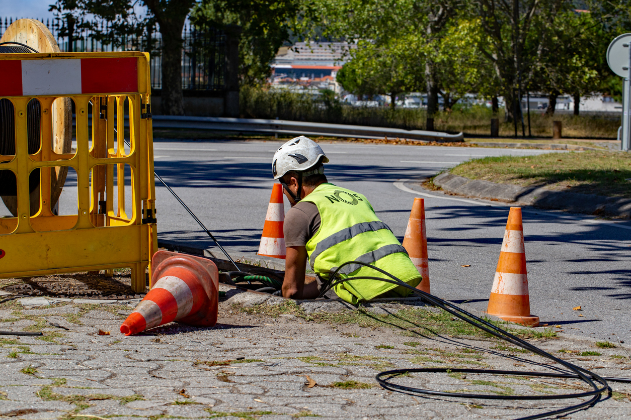 construction worker in a reflective vest working on underground cable installation with traffic cones and barriers in a sunny street setting